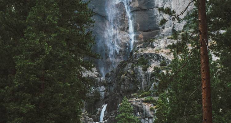 Primer plano dramático de una cascada de Yosemite cayendo entre paredes de granito oscuro enmarcada por pinos.