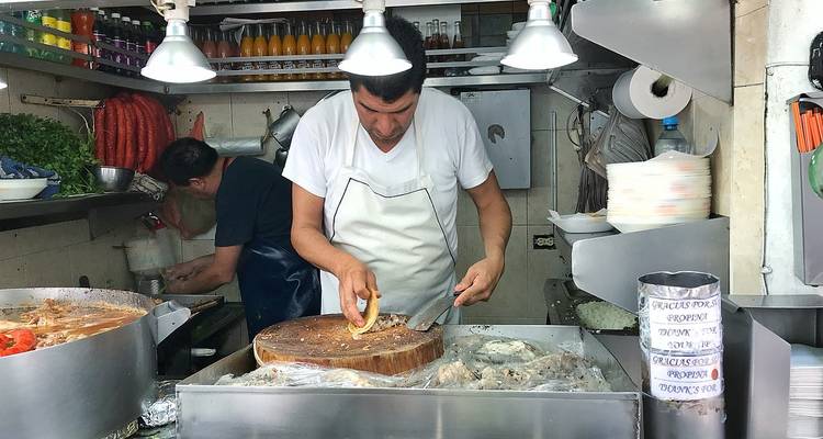 Straßenverkäufer, der Fleisch auf einem Holzblock in einem belebten Taqueriastall in Mexiko-Stadt schneidet.