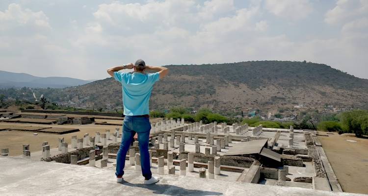 Mann betrachtet Panoramablick auf antike Steinruinen und umliegende Hügel von einer hohen Terrasse aus.
