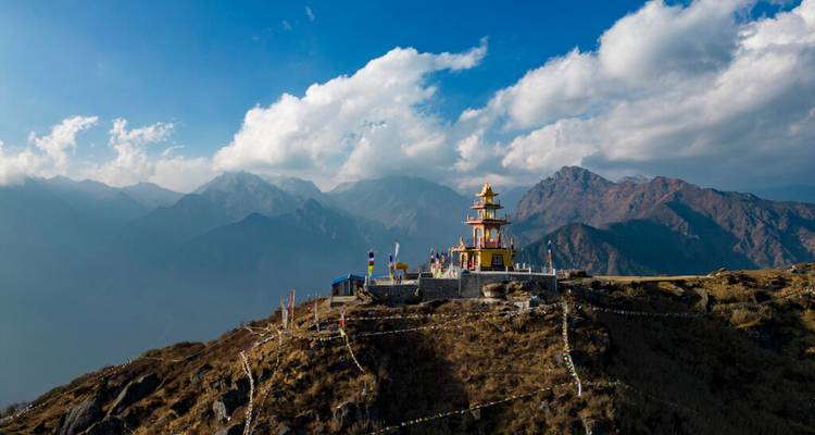 Kleurrijke stupa op een hoge bergkam omlijst door dramatische Himalaya-toppen onder een diepblauwe hemel.