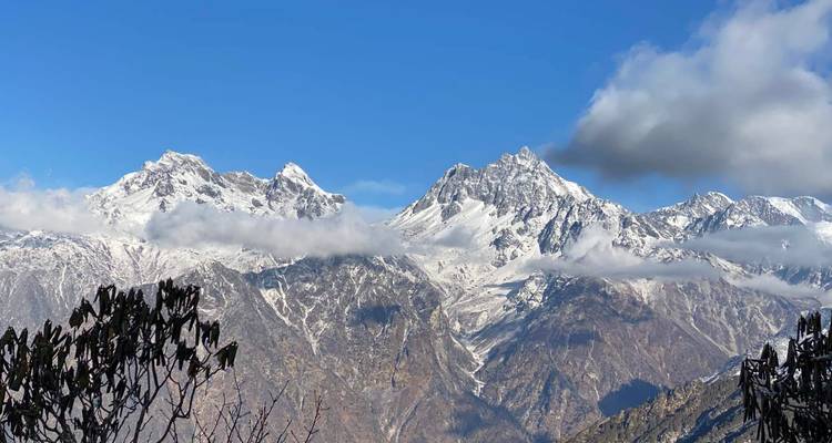 Sneeuwbedekt Himalaya-massief omlijst door sluiers van wolken onder een levendige blauwe hemel.