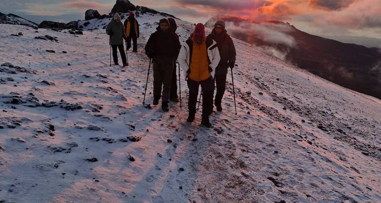 Hikers pause on a rosy snow slope at dawn with mist rising from the valley.