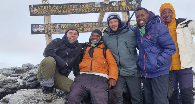 Group of climbers beam at the iconic Uhuru Peak summit sign.