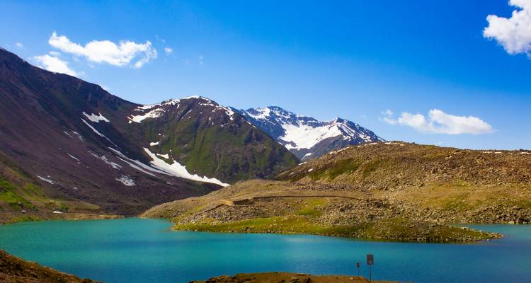 Lago alpino turquesa enmarcado por montañas escarpadas con picos nevados bajo un cielo azul despejado.