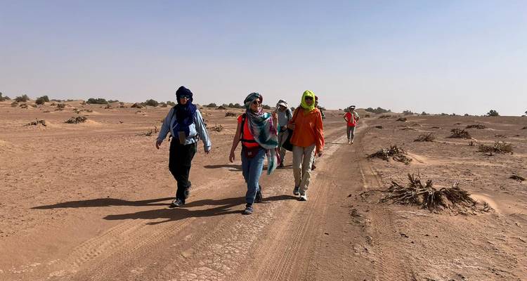 Wandelaars met hoofddoeken lopen over een door de zon geblakerd Marokkaans woestijnpad onder een heldere hemel.