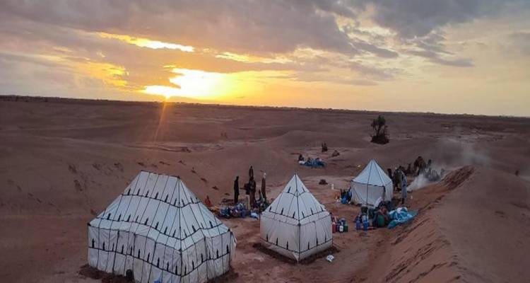 Witte nomadententen en uitrusting opgezet op woestijnkam bij dramatische zonsopgang met gouden wolken.