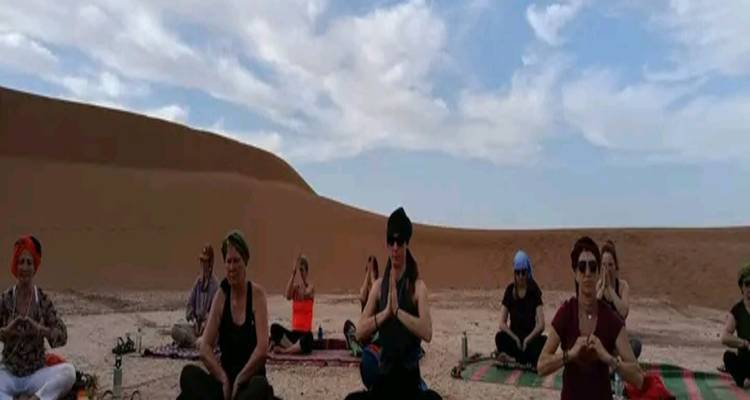 Groepsyogasessie in een kaarsenring op woestijnzand onder het vroege ochtendlicht.