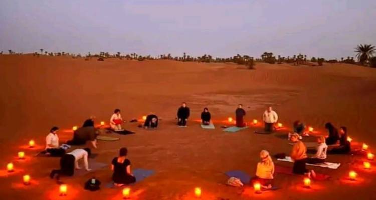 Los participantes practican posturas de yoga en un círculo iluminado con velas en el suelo del desierto al amanecer.