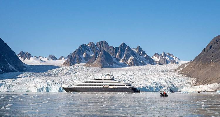 Yacht d'expédition de luxe ancré devant un vaste glacier et des montagnes déchiquetées dans l'Arctique.