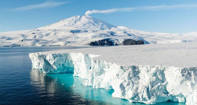 Plateforme glaciaire blanc brillant avec eau turquoise en dessous d'un volcan couvert de neige s'élevant majestueusement