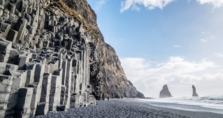 Falaises de colonnes de basalte et plage de sable noir à Reynisfjara avec des pitons rocheux s'élevant au large.
