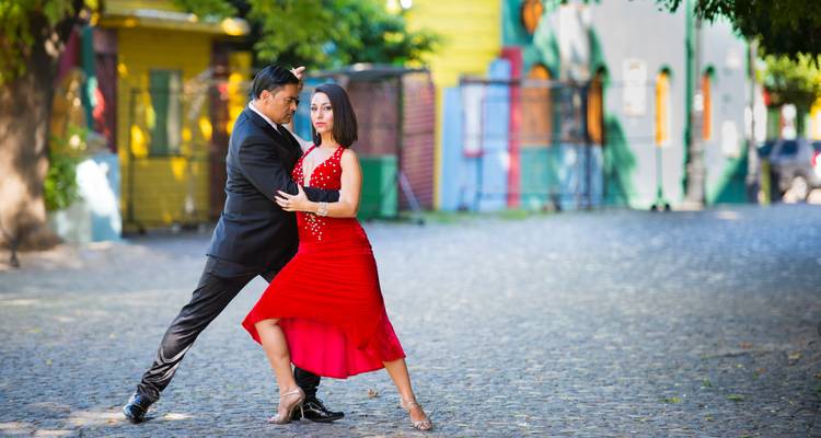 Elegantes Paar tanzt Tango auf einer Kopfsteinpflasterstraße, gesäumt von bunt bemalten Gebäuden.