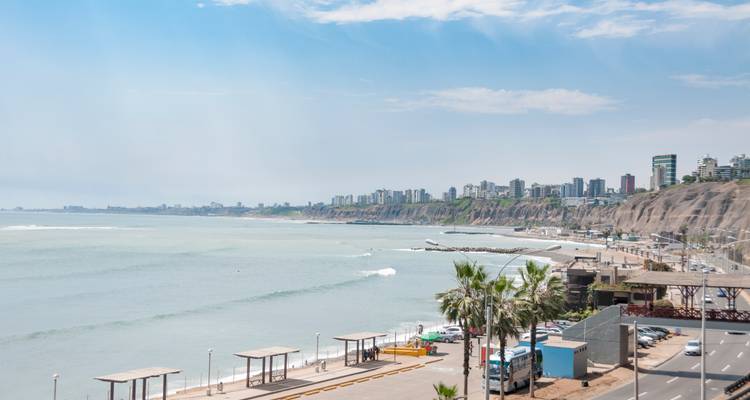 Vue panoramique de l'autoroute côtière de Lima, des spots de surf et de l'horizon moderne perché sur les falaises sous un ciel brumeux.