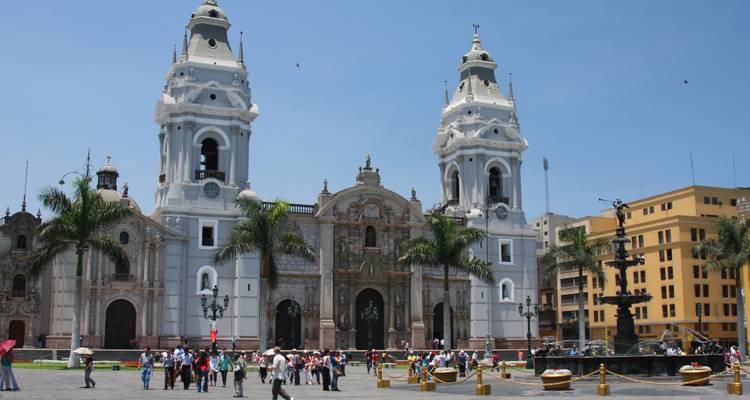 La cathédrale historique de Lima domine la Place de la Cathédrale avec des foules de visiteurs et des palmiers sous un ciel bleu éclatant.