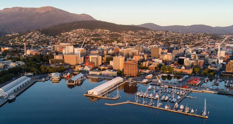Vue aérienne de la marina du front de mer de Hobart et de la ville encadrée par des montagnes boisées à la lumière de l'aube.