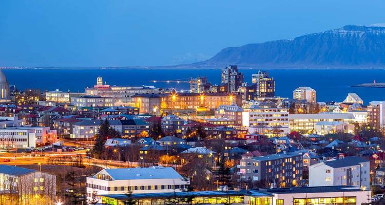 Twilight panorama of Reykjavik’s colorful cityscape backed by snow-topped Mount Esja and Faxa Bay.