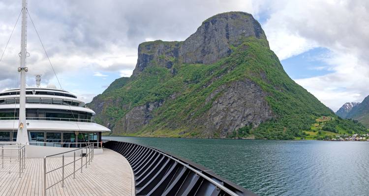Modernes Kreuzfahrtschiff gleitet durch einen schmalen norwegischen Fjord mit steilen grünen Bergklippen.