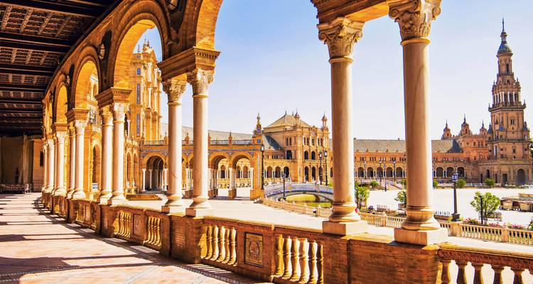 Sonnenbeschienene Bögen und gefliester Platz der Plaza de España in Sevilla mit verzierten Türmen und blauem Himmel.