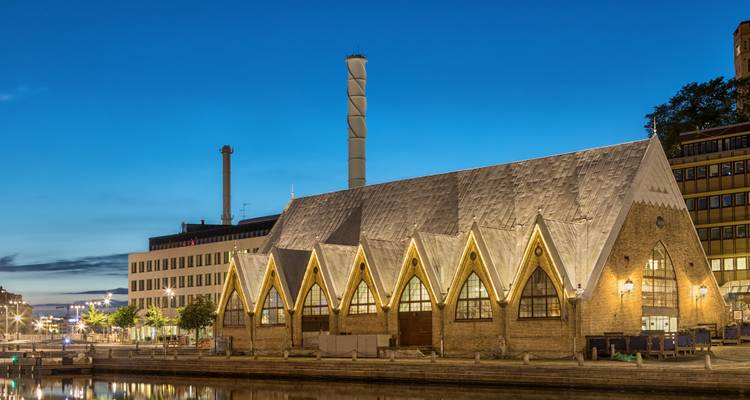 Abendansicht der beleuchteten Fischmarkthalle Feskekôrka in Göteborg am Kanal unter tiefblauem Himmel.