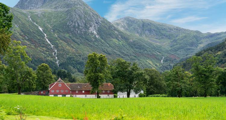 Une grange rouge sur des champs verts sous les pentes dramatiques des montagnes norvégiennes avec des cascades