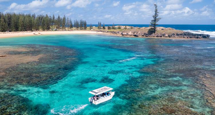 Clear turquoise lagoon at Norfolk Island with glass-bottom boat and pine trees