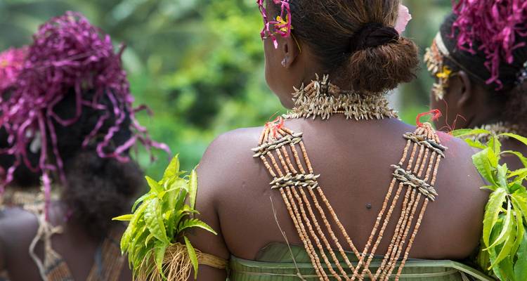 Vue rapprochée de femmes vêtues de costumes traditionnels vibrants des îles du Pacifique, ornés de coquillages et de feuillage coloré, se préparant pour une danse culturelle.