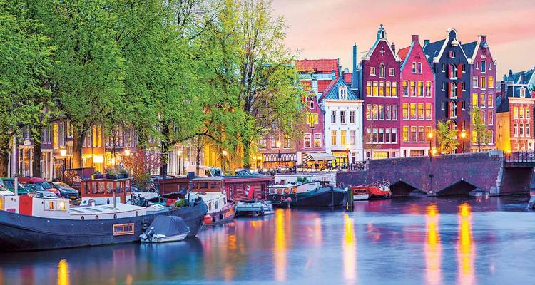 Les maisons colorées aux canaux d'Amsterdam et les bateaux amarrés brillant au crépuscule se reflétant dans l'eau.