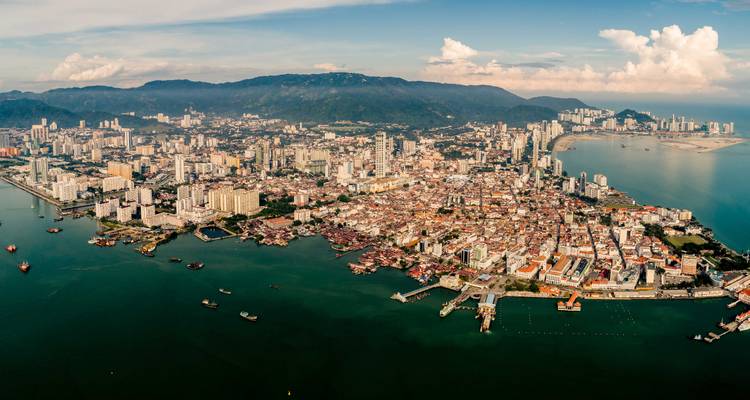 Panoramisch luchtfoto van George Town op Penang Island, Maleisië, met dicht bebouwde skyline die uitsteekt in smaragdgroene wateren.