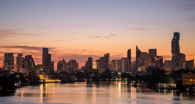 Bangkoks Stadtsilhouette bei Sonnenuntergang, die sich im Chao Phraya Fluss mit pastellfarbenem Himmel spiegelt.