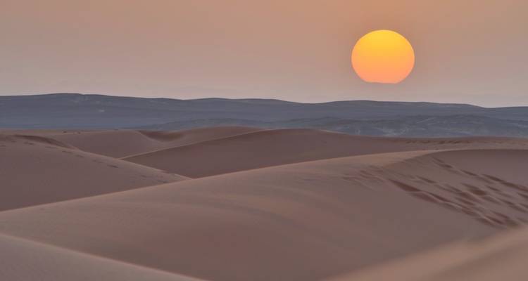 Goldene Sonne, die über glatten Sanddünen der Sahara untergeht und geschichtete Silhouetten erschafft.