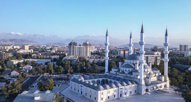Luftaufnahme der Skyline von Bischkek mit großer weißer Moschee und entfernten Gipfeln.