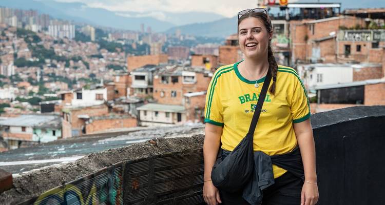 Glimlachende vrouw in geel Brazilië shirt met uitzicht op het stadsbeeld van Medellín.