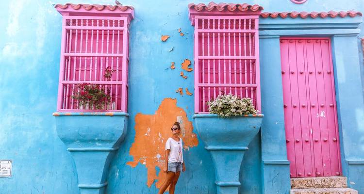 Reiziger poseert bij levendige roze en blauwe koloniale gevel in Cartagena.