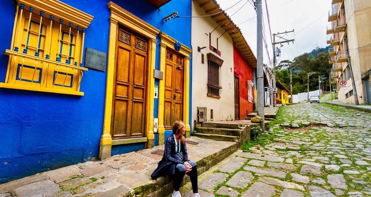 Reiziger zit op geplaveide straat naast kleurrijke koloniale huizen in Bogotá.