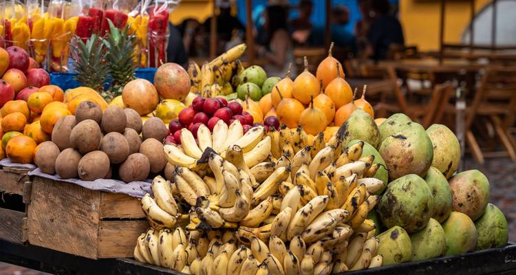 Un étal de fruits coloré dans un marché de rue rempli de bananes, de mangues et de produits tropicaux.