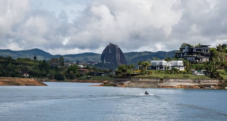 Un monolithe de granit massif s'élève au-delà d'un lac tranquille et de collines verdoyantes.