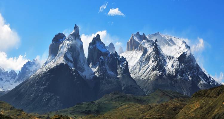 Panoramablick auf die schneebedeckten Gipfel der Cuernos del Paine vor einem tiefblauen patagonischen Himmel.