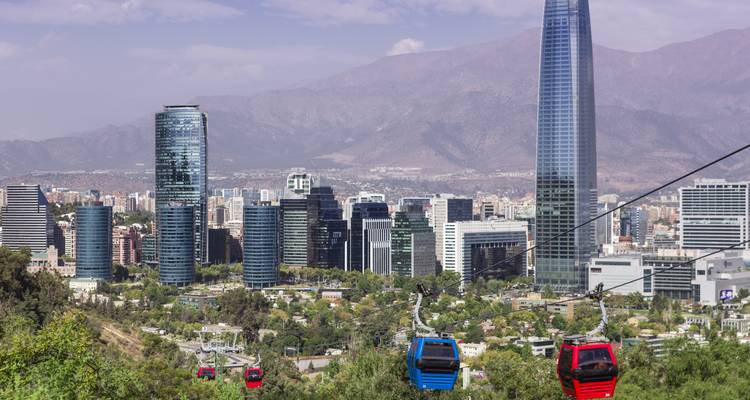Bunte Seilbahnen gleiten über grüne Hügel in Richtung Santiagos moderner Skyline vor der Kulisse nebelverhangener Andengipfel.