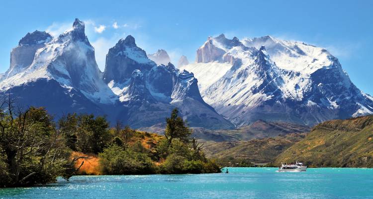 Die markanten Granithörner der Torres del Paine ragen über türkisfarbene Gewässer empor, wo ein Ausflugsboot kreuzt.