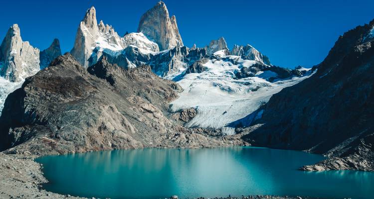 Ein türkisfarbener Gletschersee liegt unter den hoch aufragenden Granitspitzen des Fitz Roy unter klarem Himmel.