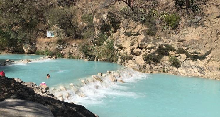 Piscinas termales turquesas en un cañón rocoso con un nadador disfrutando del agua tibia mientras pequeñas cascadas caen por escalones de piedra.