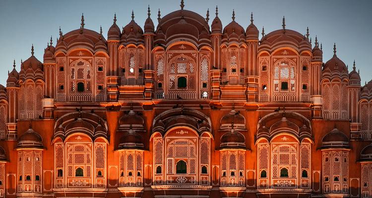 Intricately carved pink sandstone palace façade illuminated against the early evening sky.