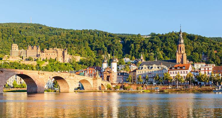 Malerische Aussicht auf Heidelberg mit der Alten Brücke, die den Neckar überquert, und Burgruinen auf einem bewaldeten Hügel.