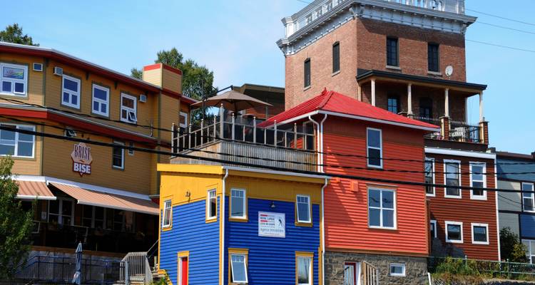 Kleurrijke houten en bakstenen gebouwen met balkons en terrassen staan langs een zonnige straat in een historische Canadese stad.