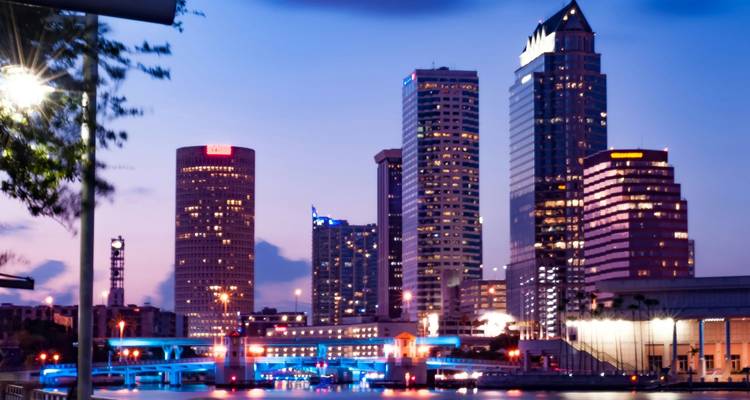 Horizonte colorido nocturno de Tampa con luces de neón azules del puente reflejándose en el agua.