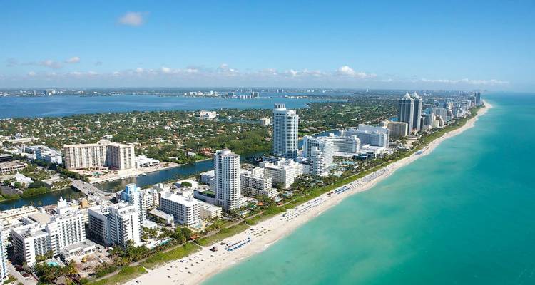 Vista aérea expansiva del paisaje urbano y la costa de Miami Beach con agua turquesa que se extiende hasta el horizonte.