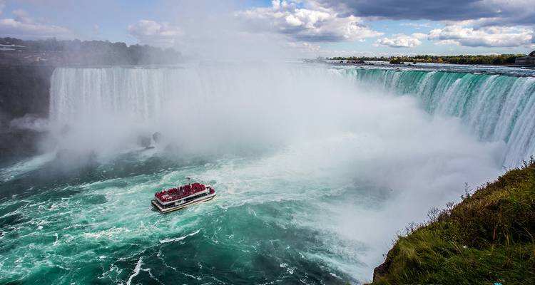 Cataratas del Niágara brumosas con aguas turquesas arremolinadas y un barco turístico acercándose a la cascada.