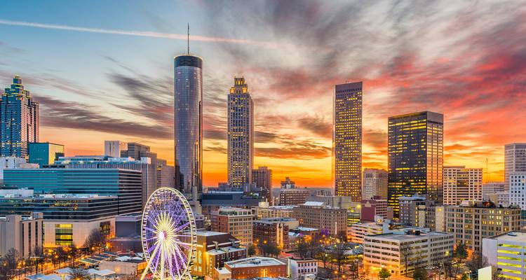 Dramatische zonsondergang boven Atlanta's stadskern met een reuzenrad en gestreepte wolken.