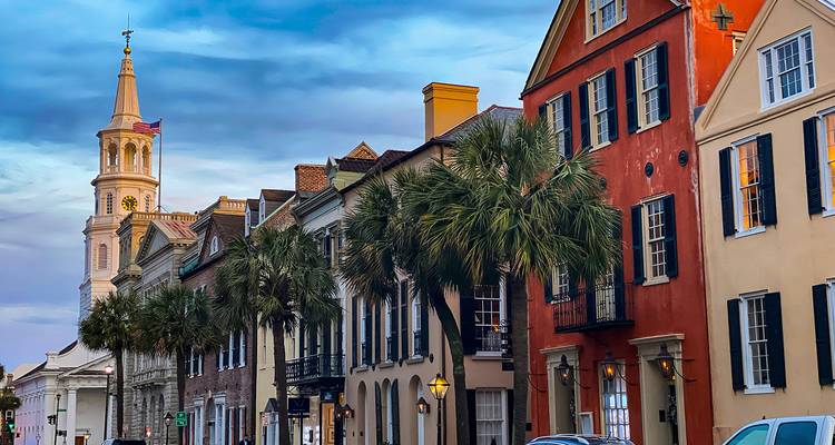Historische pastelkleurige rijtjeshuizen en kerktoren omzoomd met palmbomen in Charleston bij schemering.