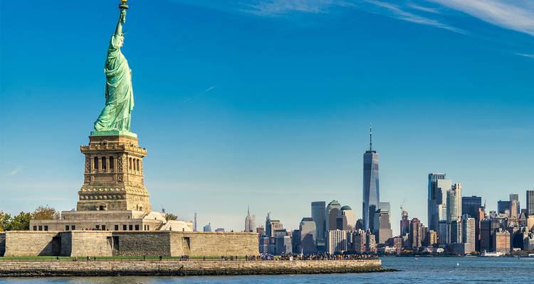 Vrijheidsbeeld met de skyline van Lower Manhattan aan de overkant van een helderblauwe haven.